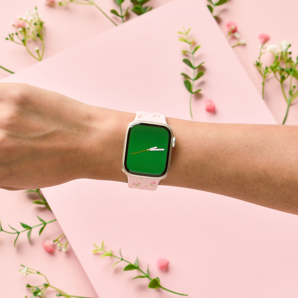 Hand wearing a pink Ditsy Floral Apple Watch strap with green smartwatch screen, surrounded by flowers.