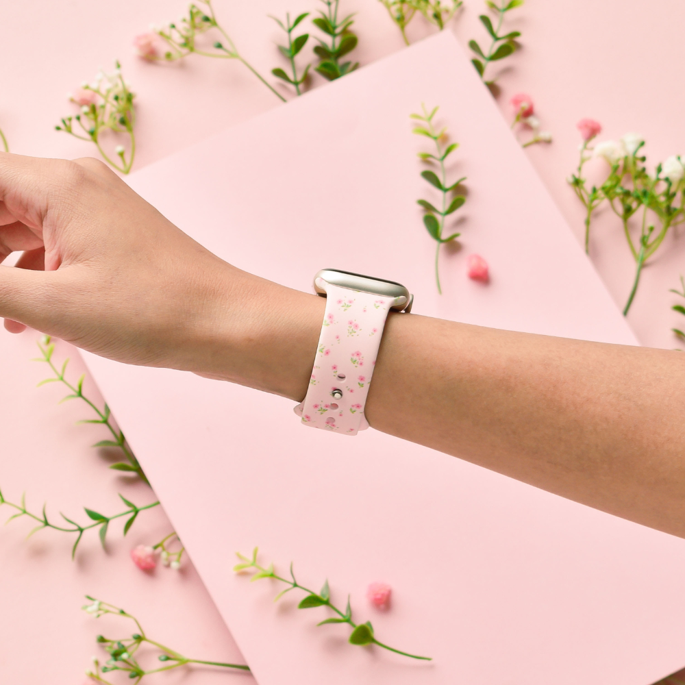 Pink Apple Watch strap with ditsy floral pattern on a wrist, pink background with small flowers.