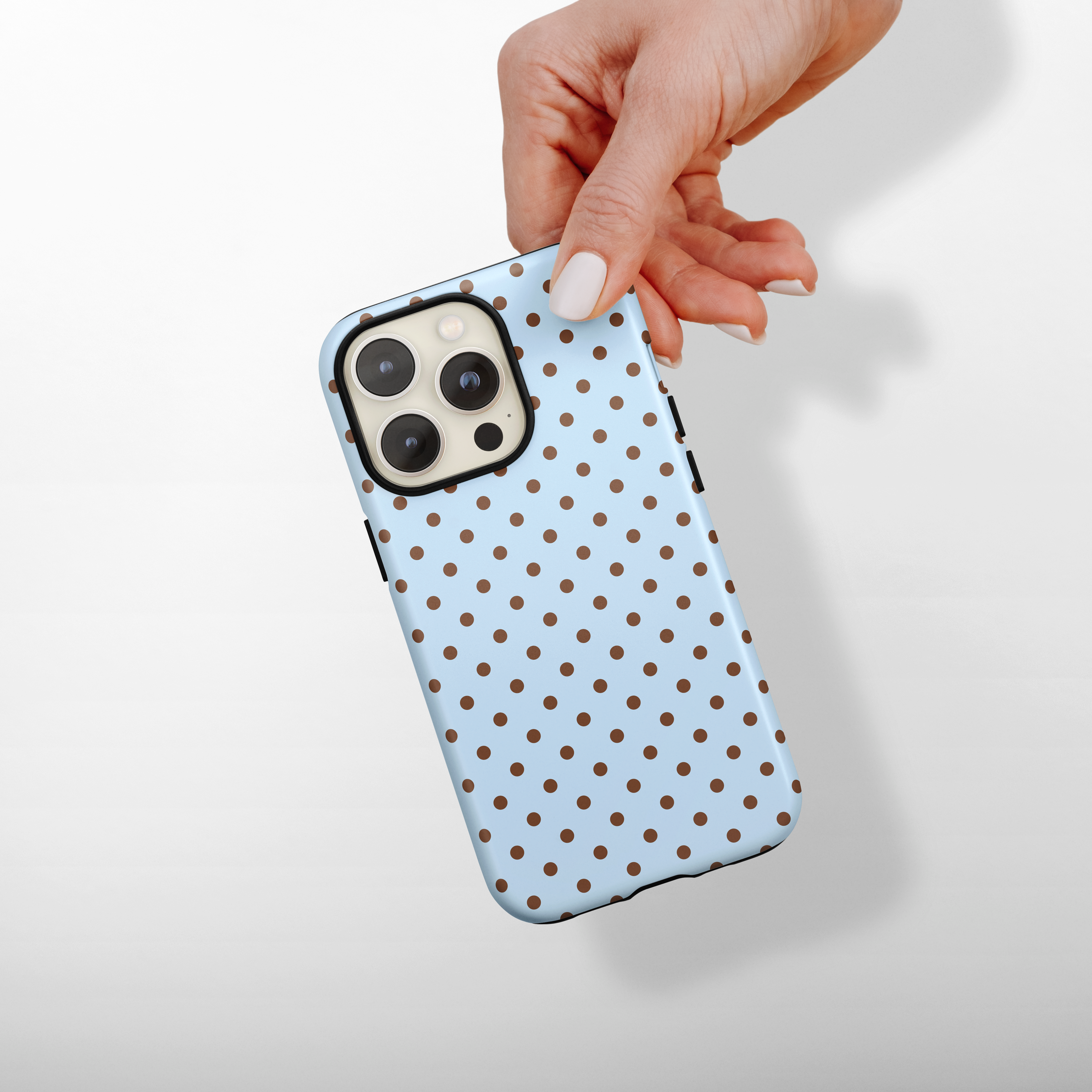 Hand holding a phone with a blue polka dot case on a light background