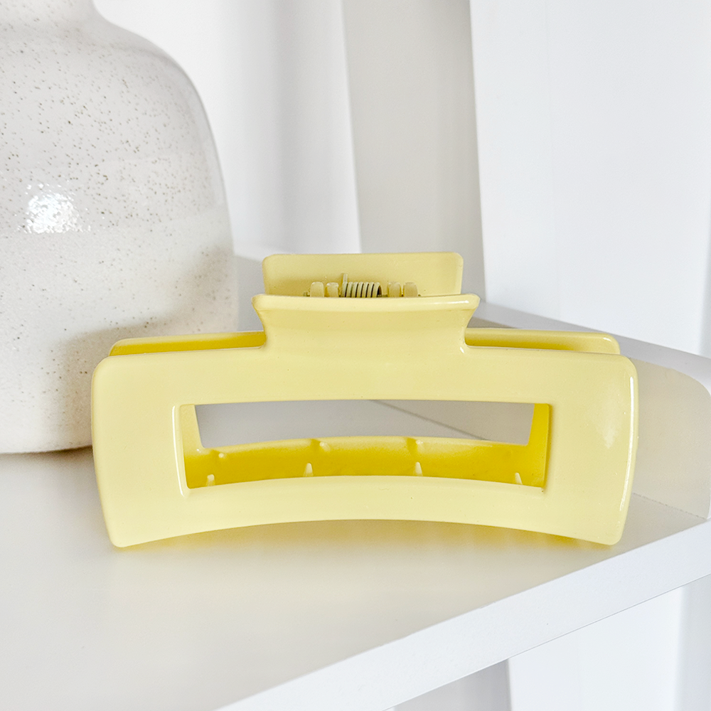 Yellow square claw clip with open design displayed on a white shelf beside a ceramic vase.