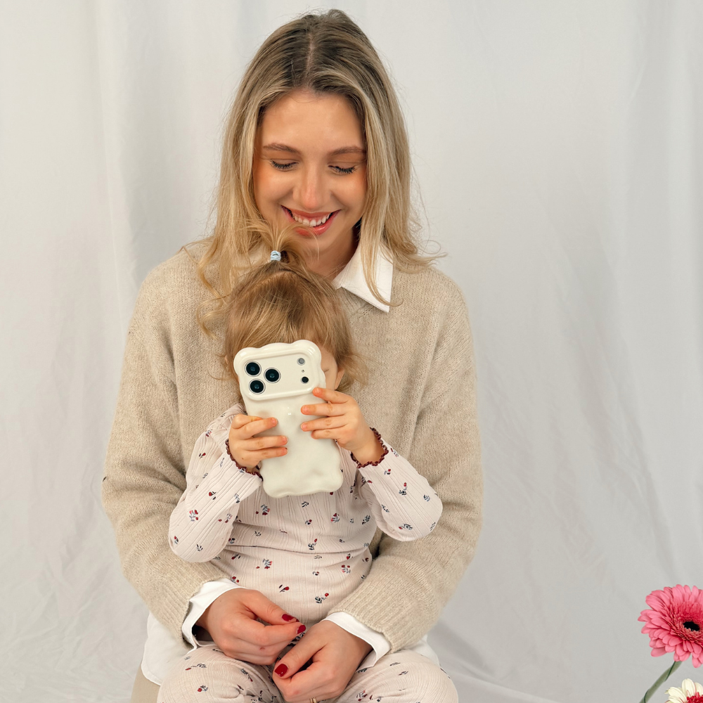A smartphone with a shiny, cream-colored case featuring a wavy, bumpy texture is placed on a light grey surface. The phone’s camera lenses are visible at the top.