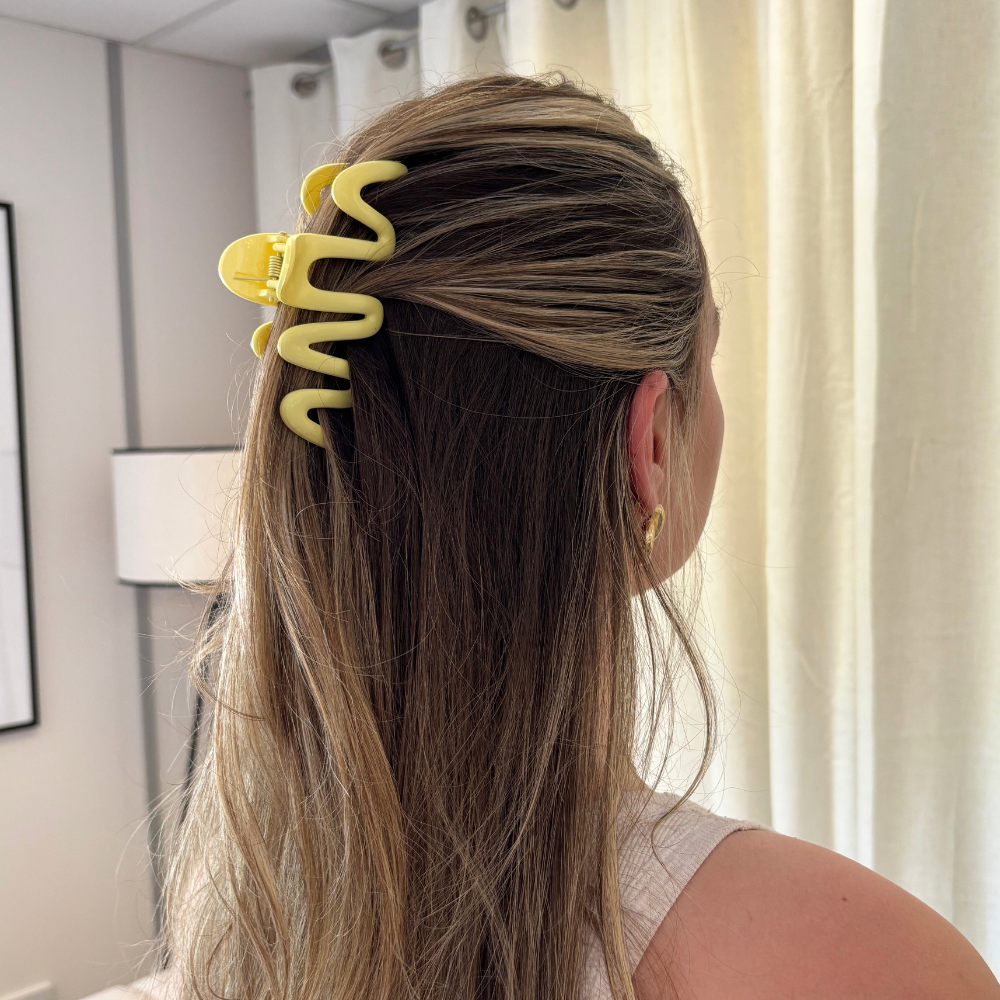Woman with long brown hair in a half-updo wearing a yellow squiggle claw clip, shown from the back.