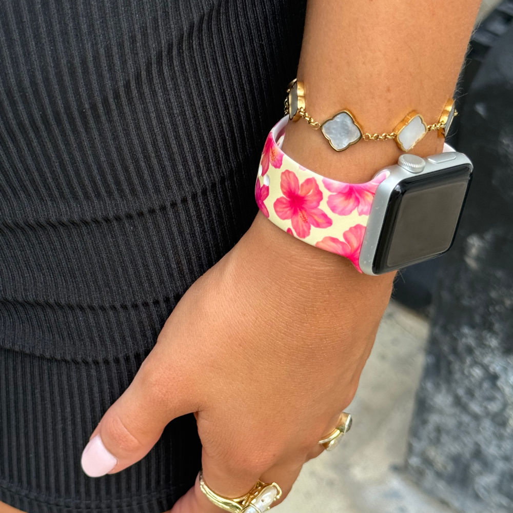 Butter yellow Apple Watch strap with hibiscus print, worn with a gold bracelet and rings on a womans wrist.