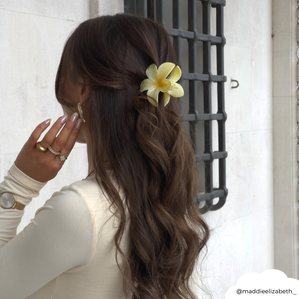 Butter yellow tropical flower claw clip secures long wavy brown hair in a half-up style.