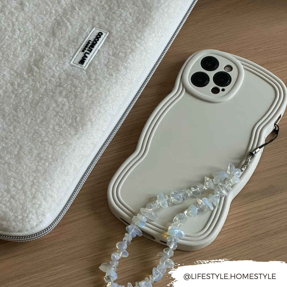 White phone with a Moonstone crystal strap and textured white case on light wood surface.