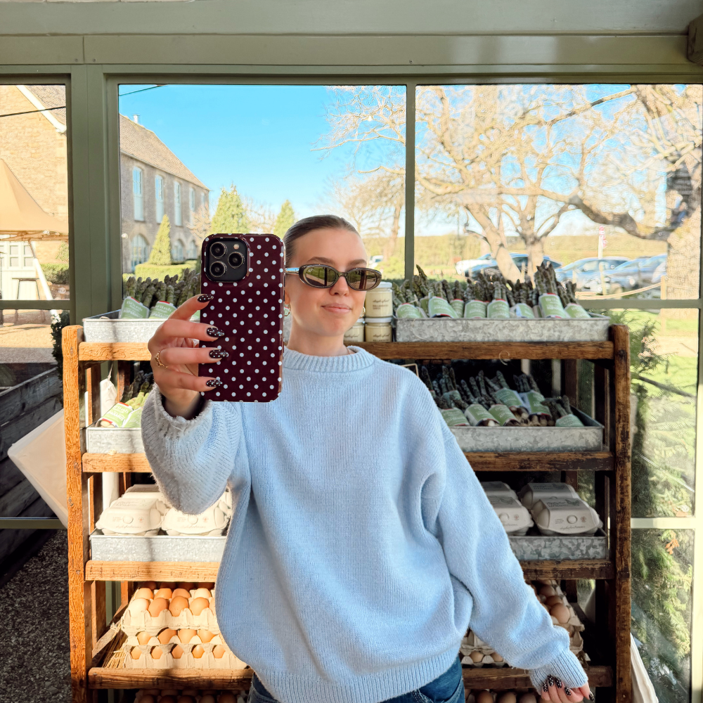 Girl holding her brown and blue polka dot phone case in hand wearing all blue in a farmshop