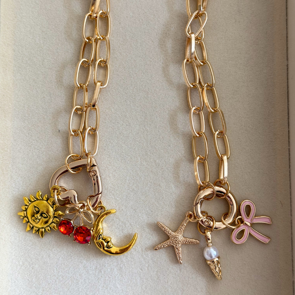 Two gold chain phone straps with various charms on a light beige background
