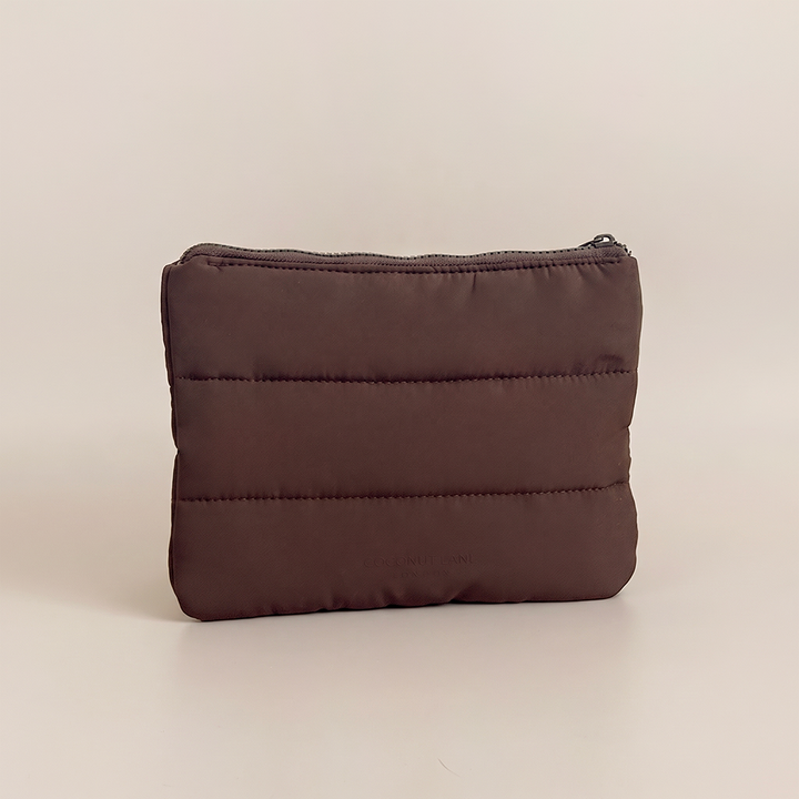 Chocolate brown padded everything pouch with horizontal quilted stitching, zip fastening and subtle Coconut Lane branding on a nude beige background.