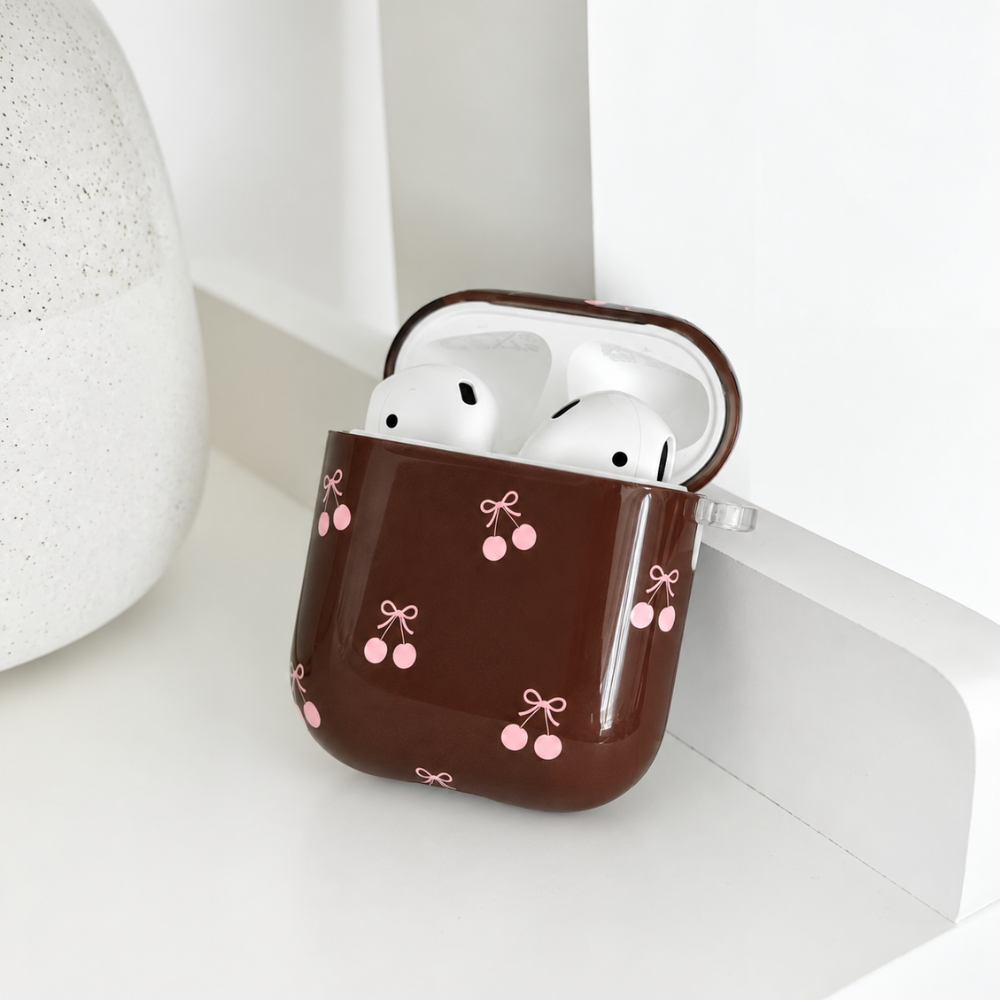 Open glossy brown AirPods case with a pink cherry and bow print, with white AirPods inside.