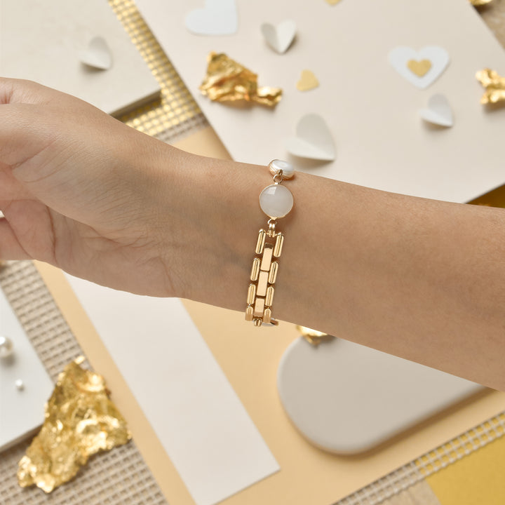 A close-up of a wrist adorned with Coconut Lane's Cute Stone Bracelet Apple Watch Strap, featuring a white gemstone charm. The background includes various decorative items such as paper hearts, gold foil pieces, and neutral-toned paper, creating a stylish and elegant setting.