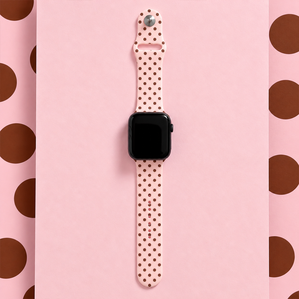 Pale pink silicone sport band with small brown polka dots, attached to a black Apple Watch smartwatch.