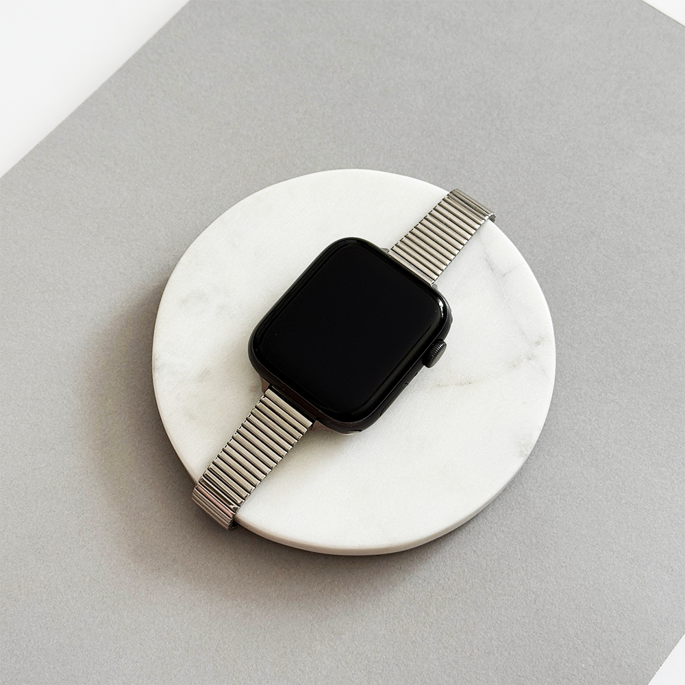 Silver Coconut Lane SLIM Fine Line Apple Watch strap displayed on a round white marble surface against a gray background.