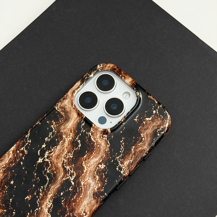 Black phone case with a swirling bronze and gold marble pattern, on a phone with three camera lenses, resting on a black surface.