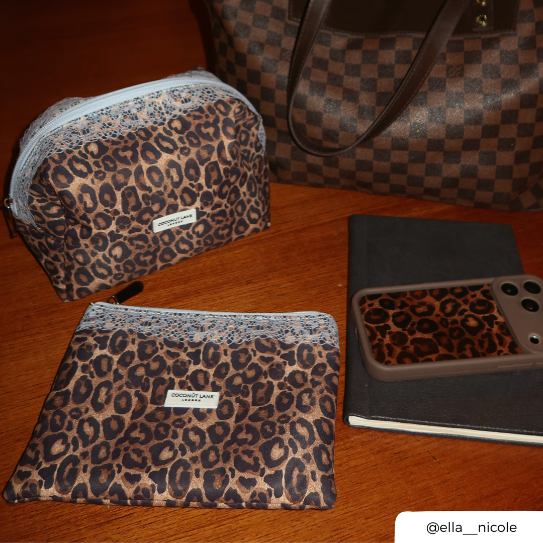 Flat lay photo on the table of the leopard print zip pouch with a pale blue lace trim along the top, a pale blue zip with a silver pull, and a white Coconut Lane London logo badge on the front, alongside the makeup bag and coconut lane mocha leopard phone case. 