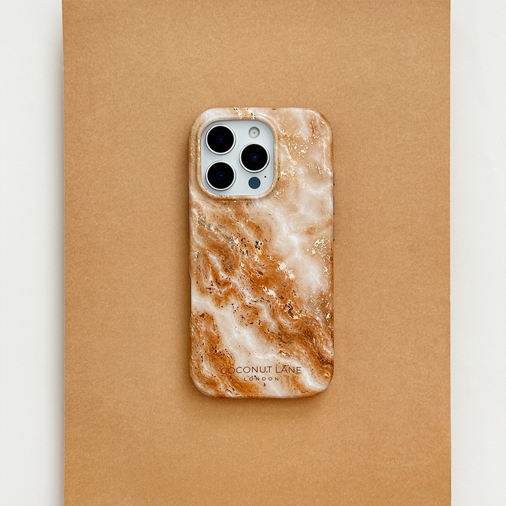 Cream and caramel marble phone case with gold veining, on a phone with three camera lenses, resting on a tan surface.