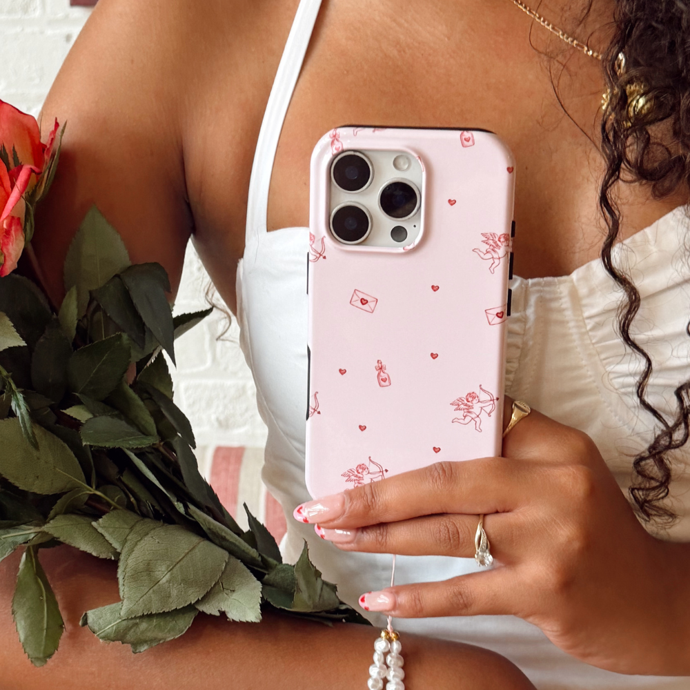 Person holding a phone with a pink case featuring cupid designs, next to roses.