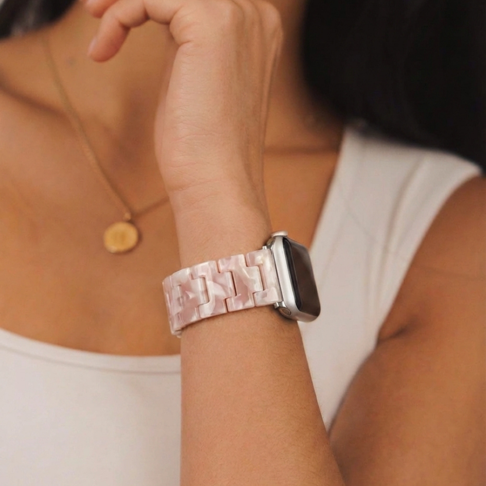 A person wears the Luxe Rose Apple Watch Strap by Coconut Lane, featuring a white, pearlescent, adjustable band on their wrist.