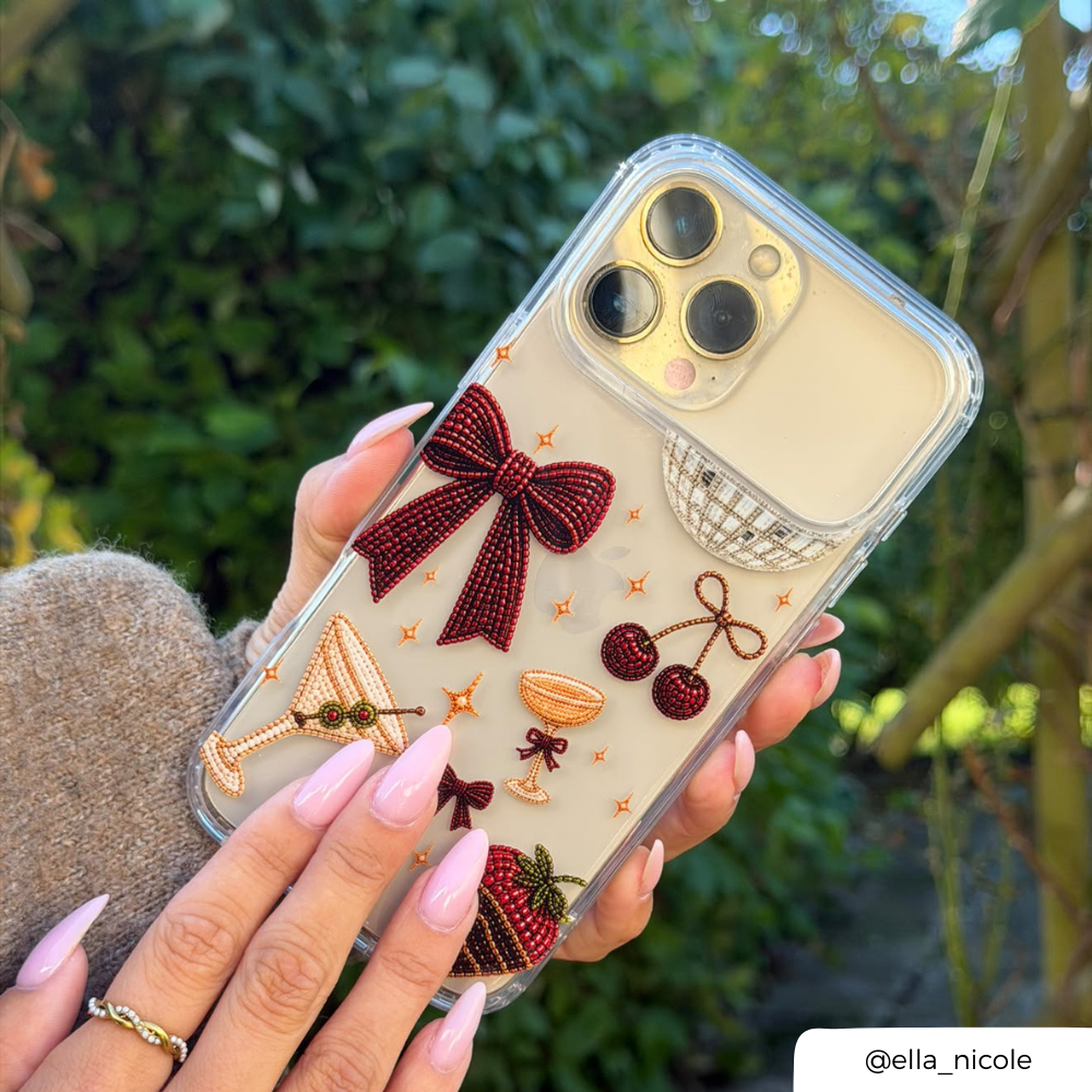 Woman holding a clear phone case decorated with a red bow, cherries, a martini glass, a strawberry dipped in chocolate, and small star accents. 