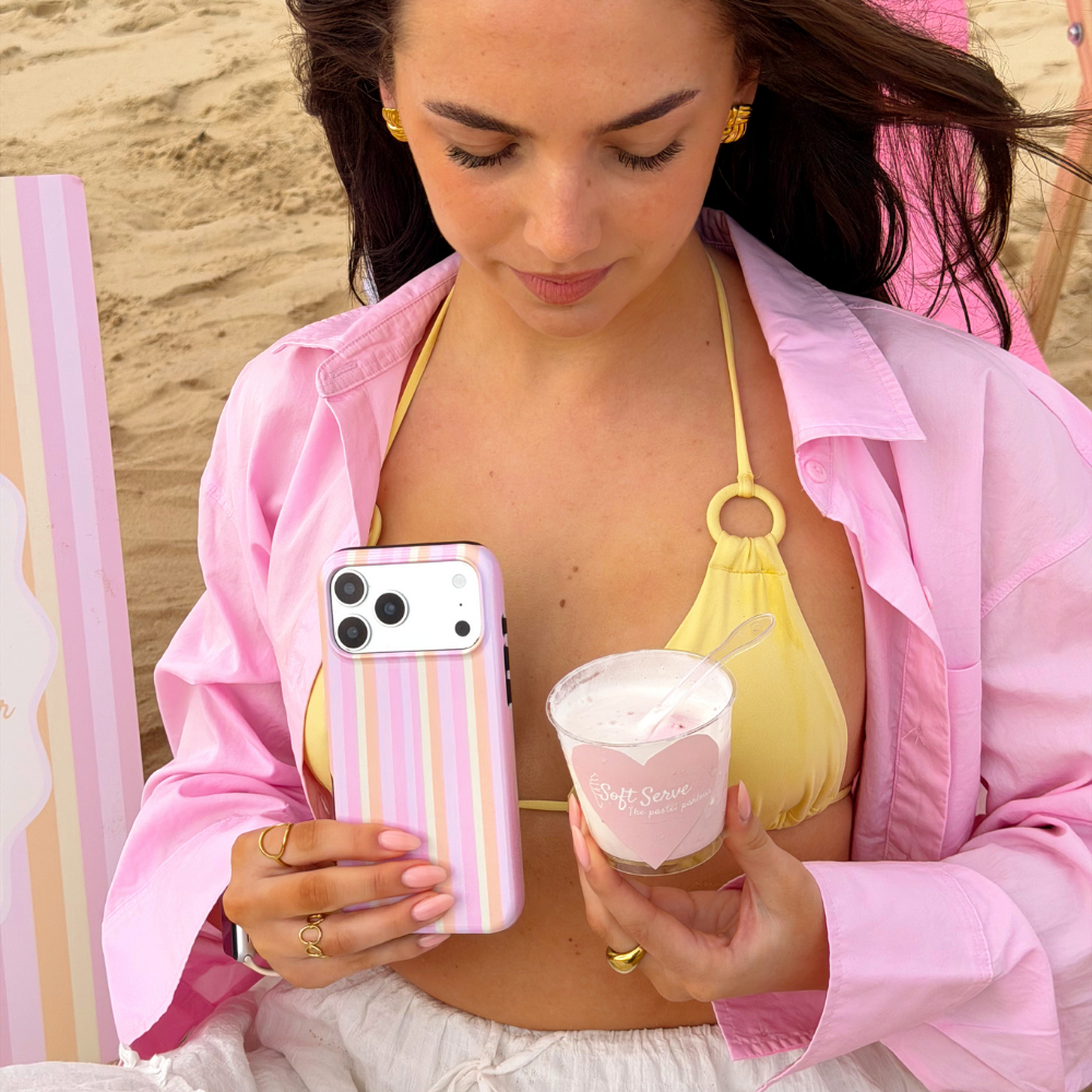 Girl on the beach wearing pink and yellow holding her pastel stripes magsafe phone case