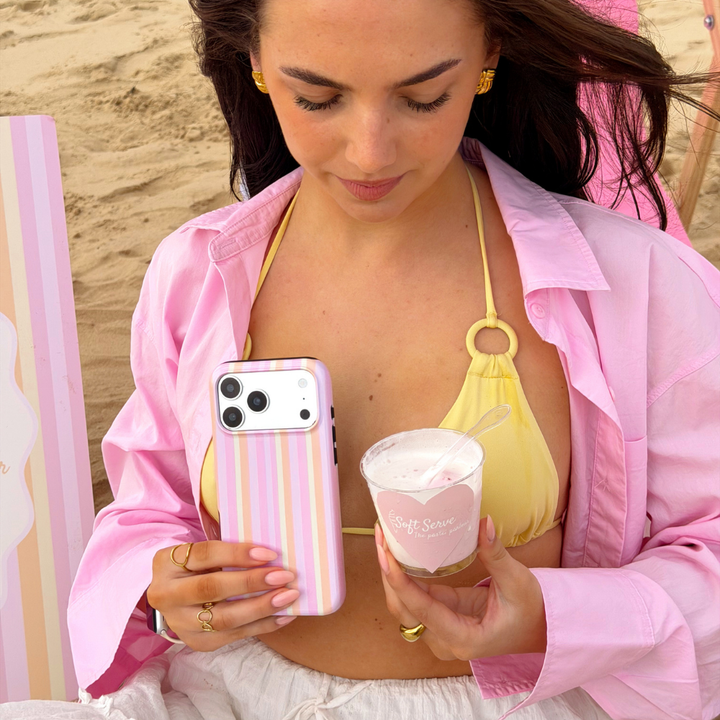 Girl on the beach wearing pink and yellow holding her pastel stripes magsafe phone case