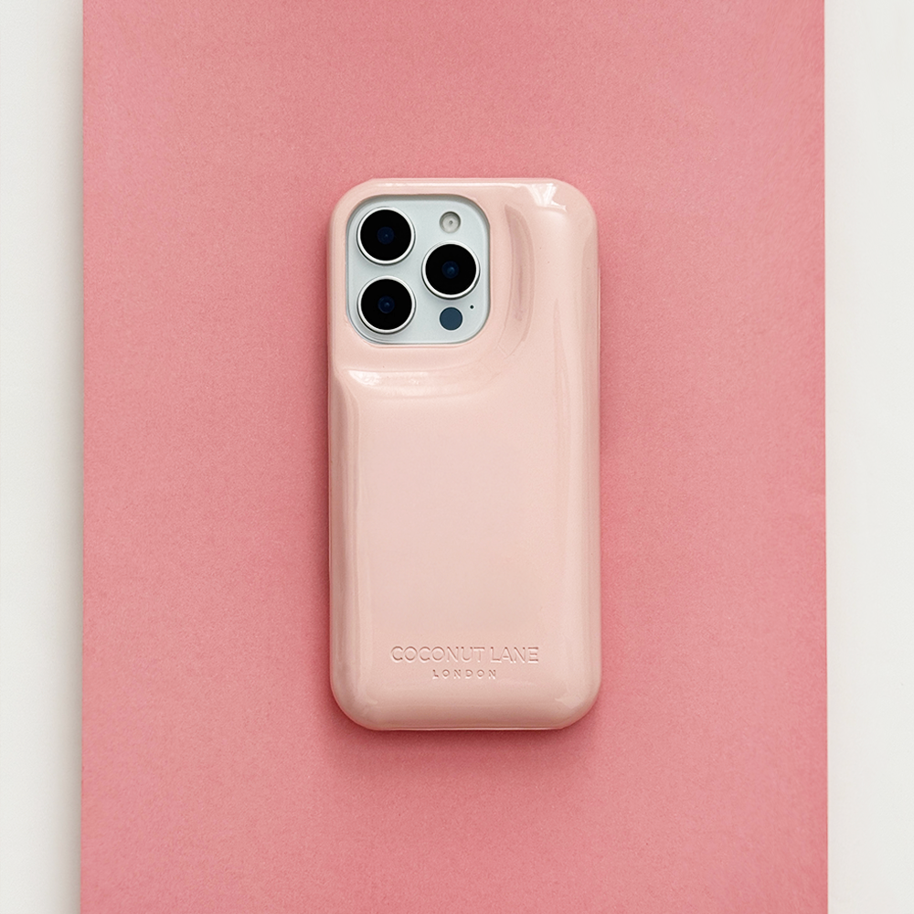 Glossy pastel pink Coconut Lane puffer phone case with embossed logo, displayed diagonally on a matching pink background.