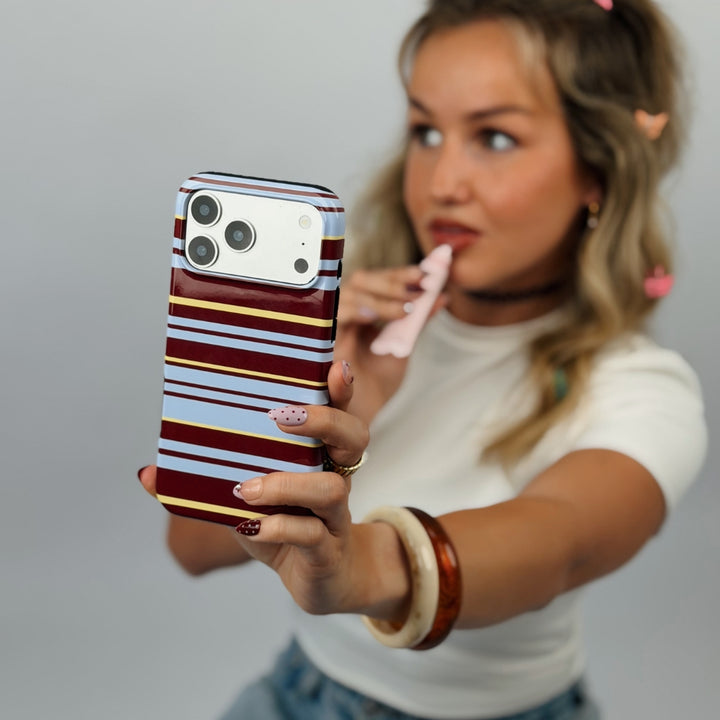 A woman holding a smartphone with Mary-Kate striped phone case featuring horizontal bands of brown, light blue, and yellow. 
