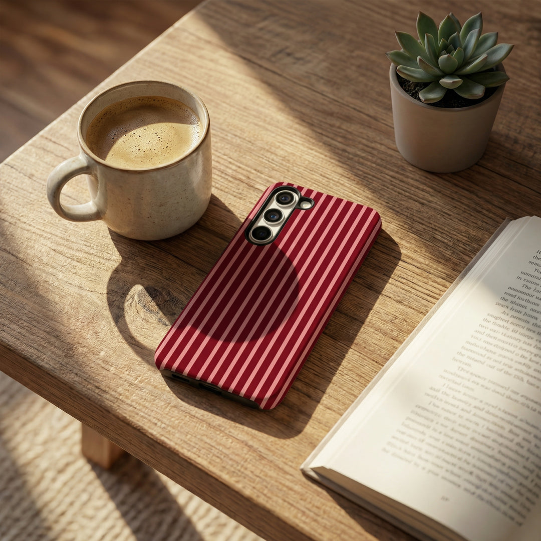 Red striped phone case on a wooden table with a cup of coffee, book, and plant.
