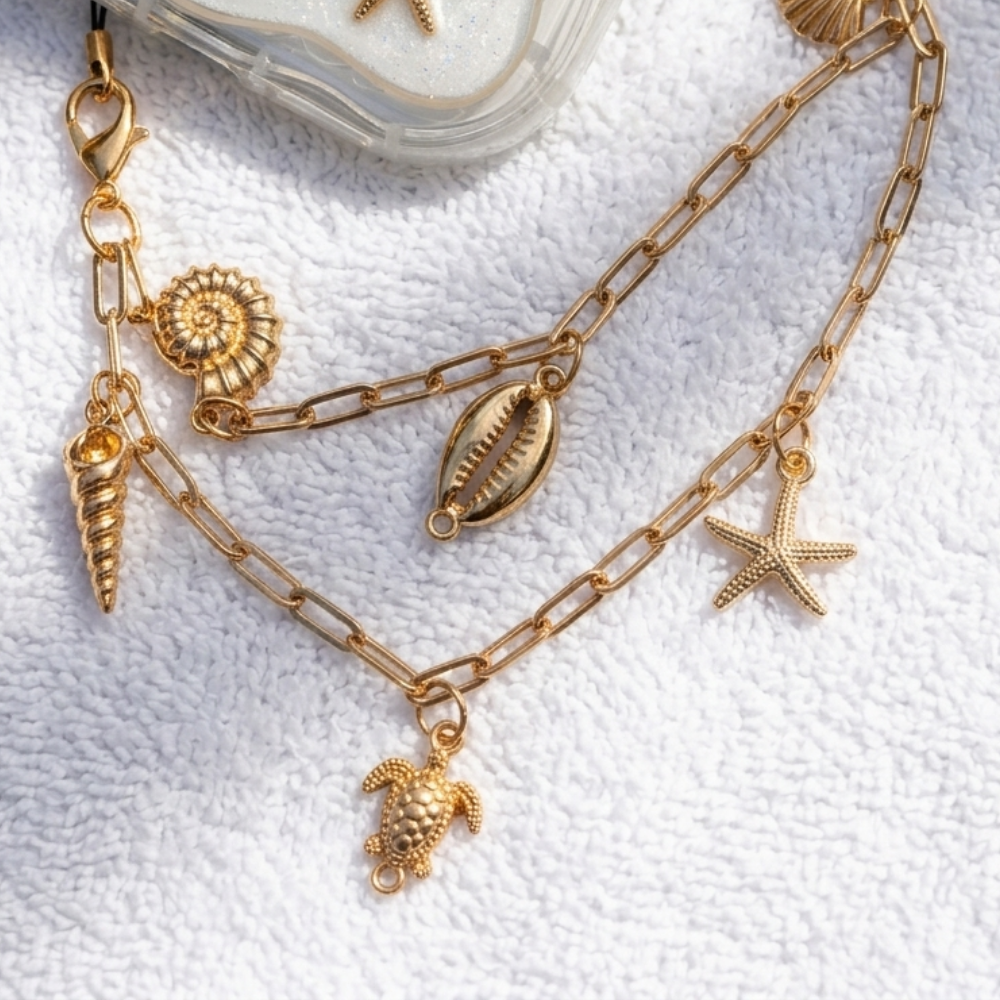 Gold chain phone strap with shell and starfish charms on a textured white surface