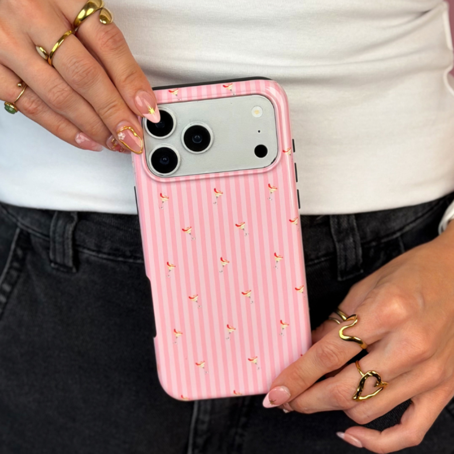 A pink striped tough magsafe phone case with small spicy margarita illustrations, held by a person wearing a white top and black jeans against a solid pink background.