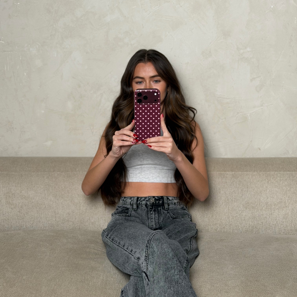 Woman holding an burgundy iphone 18 pro max,  in a burgundy tough case with baby pink polka dots. 