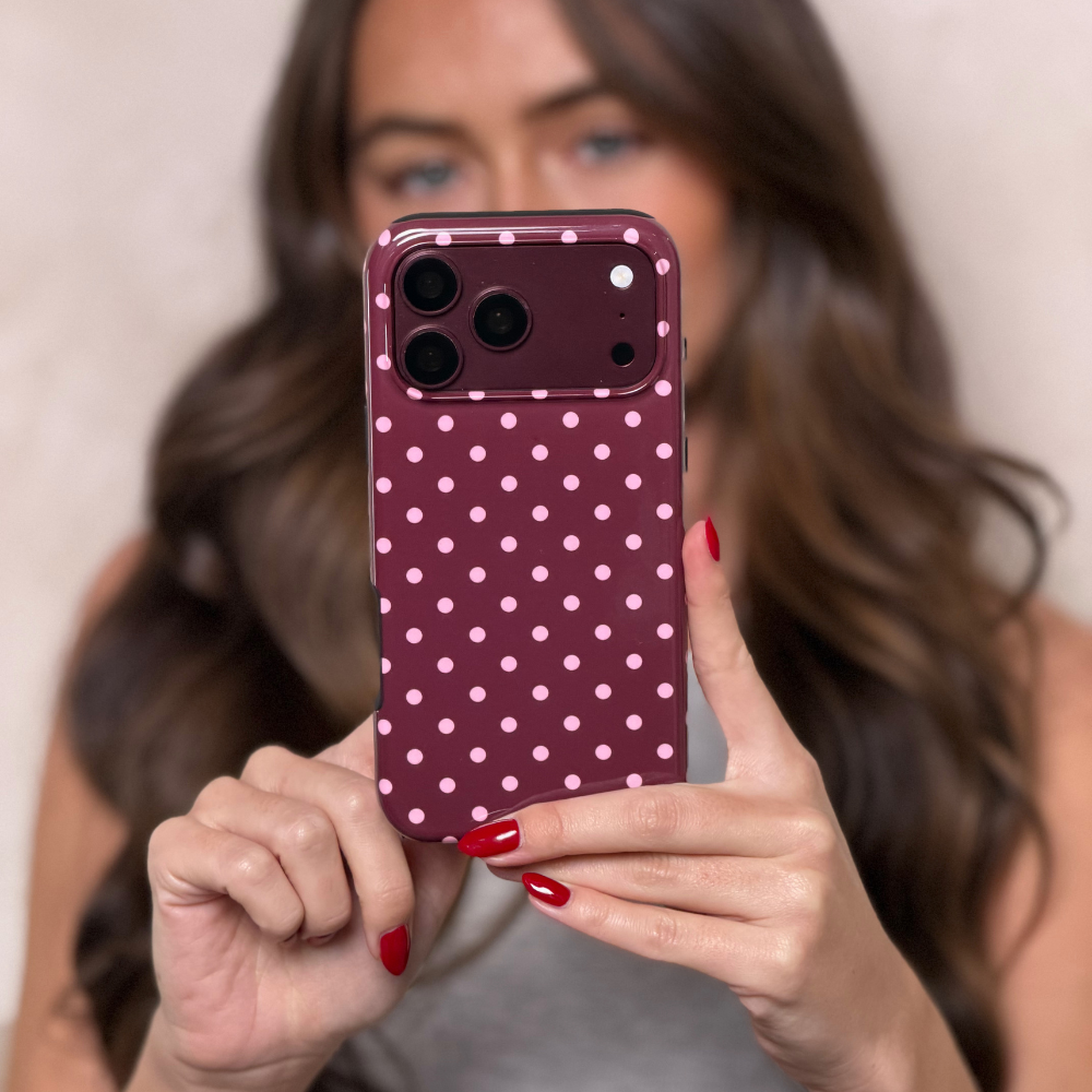 Woman holding an burgundy iphone 18 pro max,  in a burgundy tough case with baby pink polka dots. 