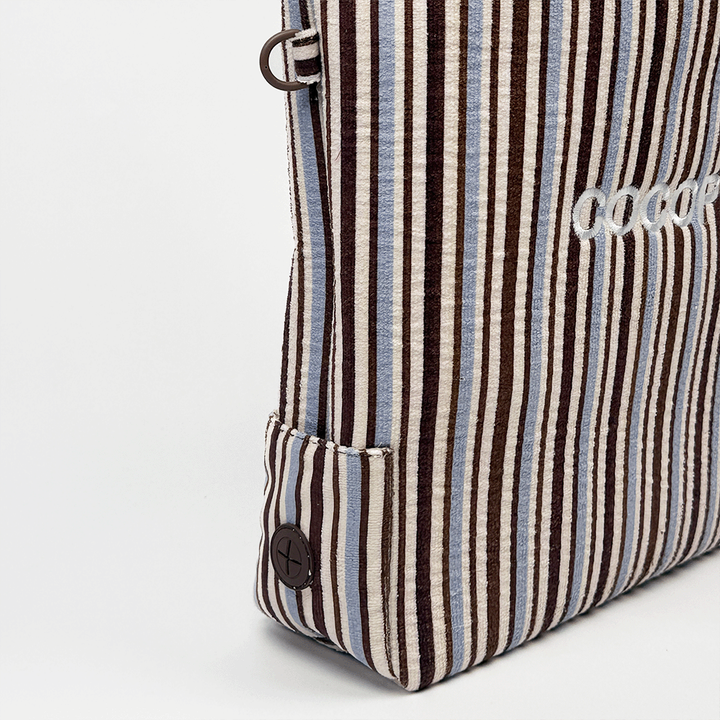 Vertical side view of a brown and blue striped tote bag with a round button at the bottom.