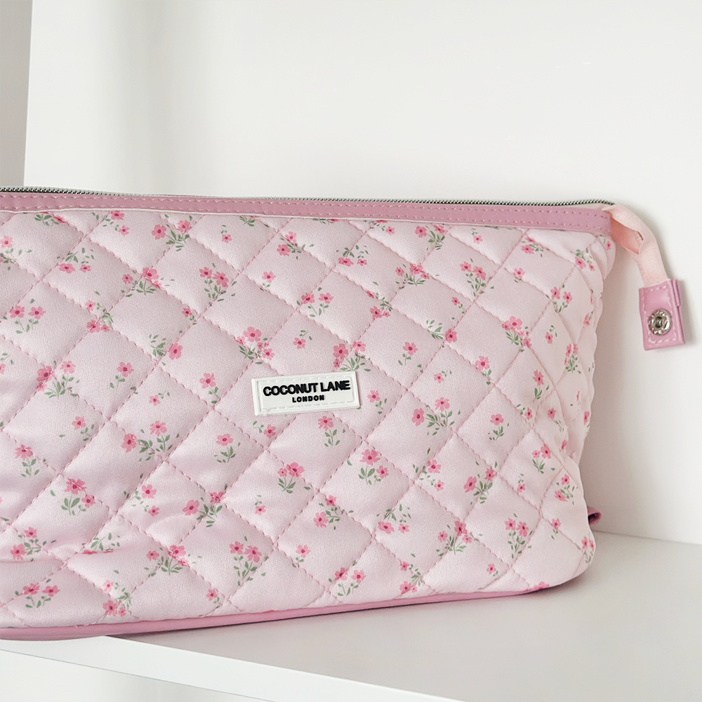 Quilted pink makeup bag with ditsy floral pattern, displayed on a white shelf.