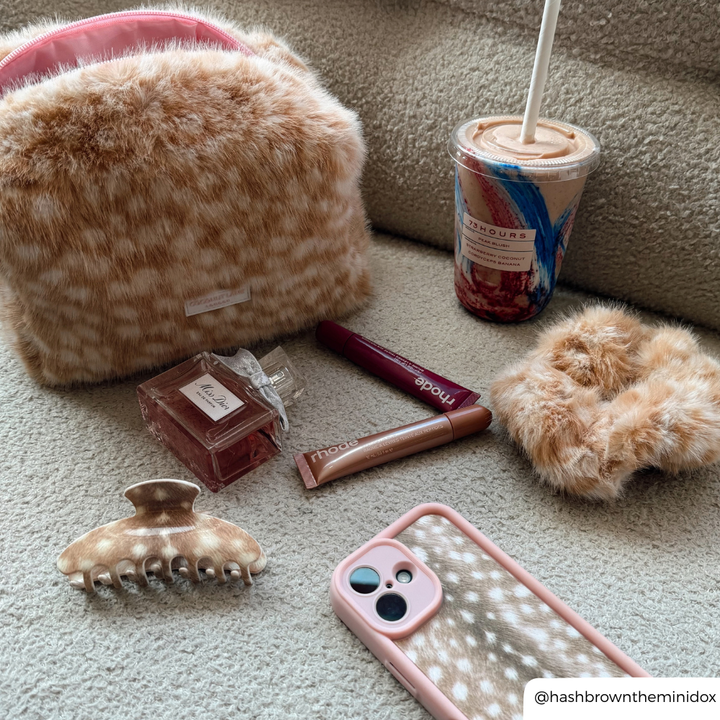 Fawn makeup products on a boucle sofa, makeup bag, claw clip, scrunchie and phone case all match
