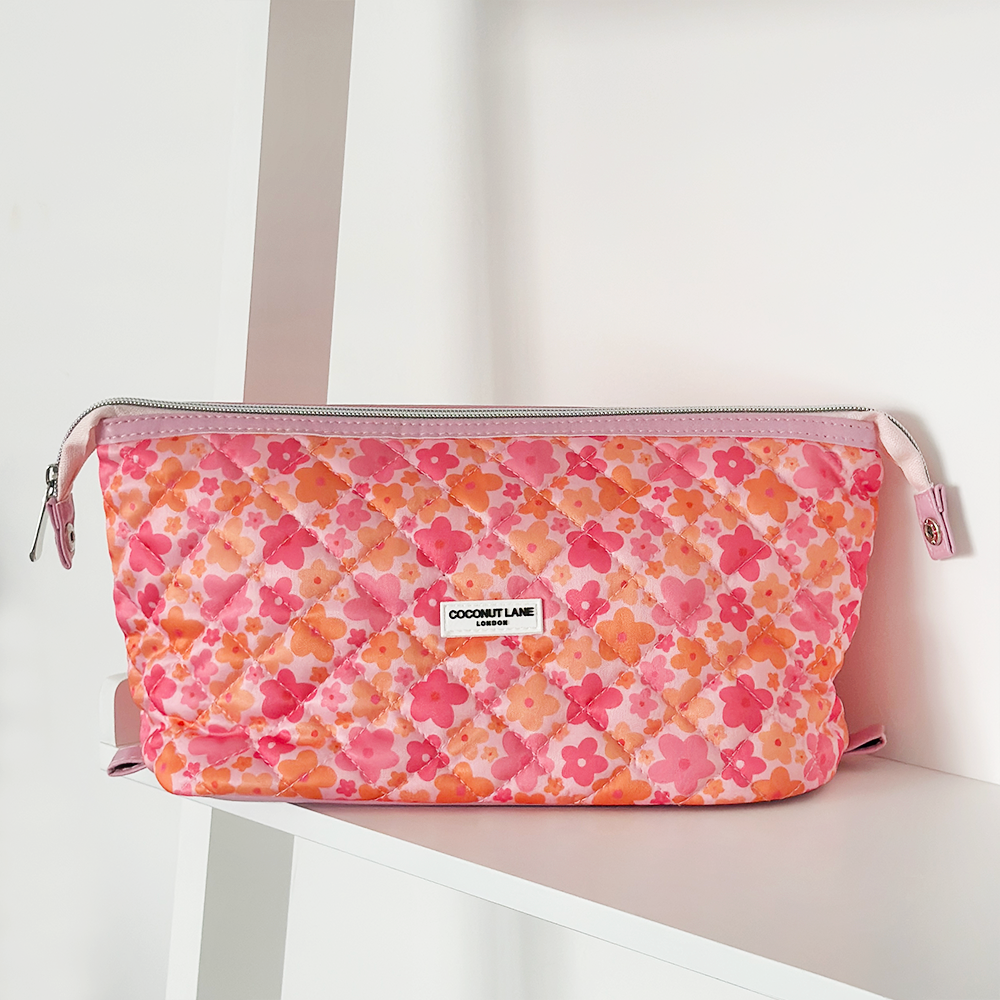 Quilted pink and orange floral expandable makeup bag by Coconut Lane on a white shelf.