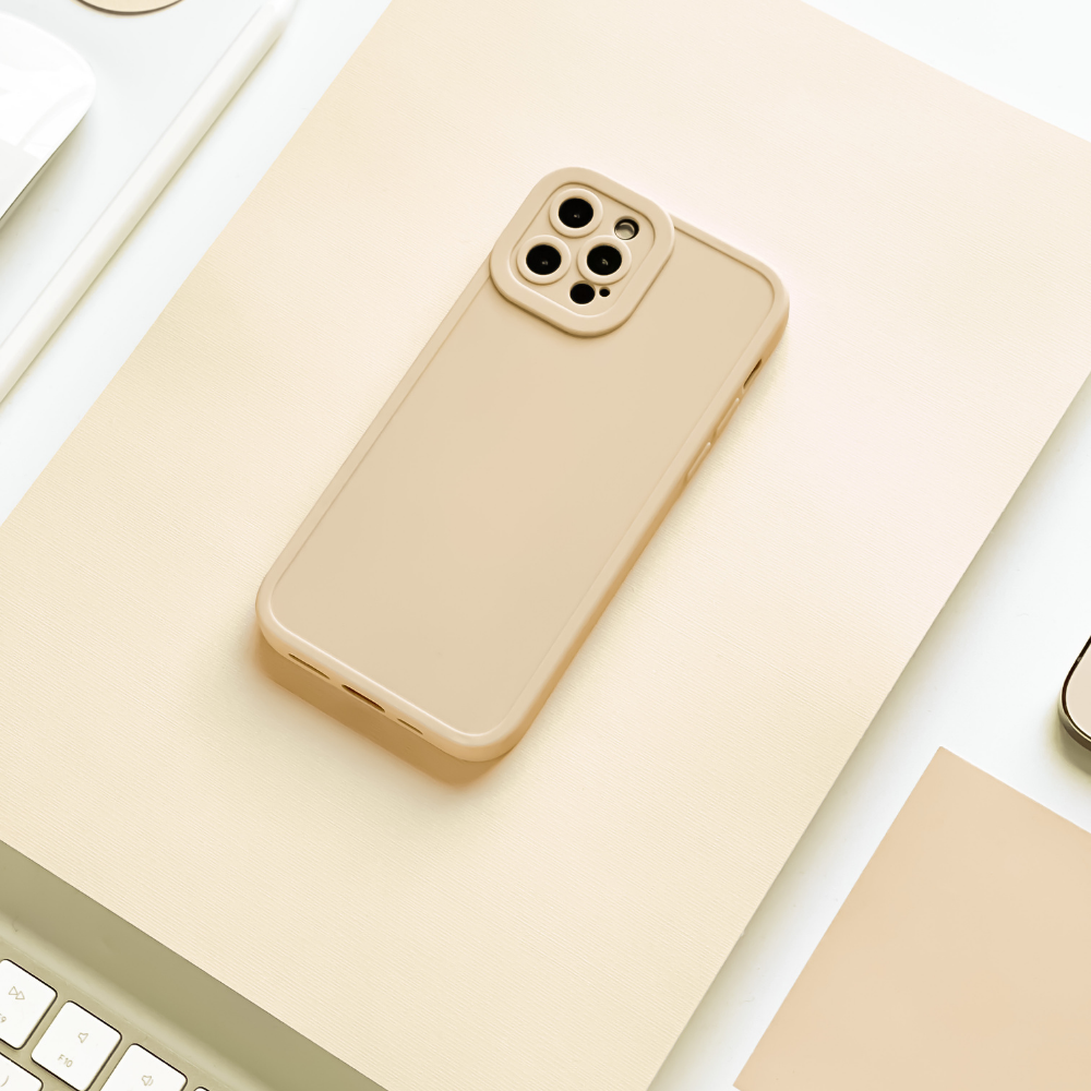 A beige smartphone with a Coconut Lane NAKD Phone Case - Nude lies flat on a cream-colored surface. Surrounding it are parts of a keyboard, a mouse, and various other office supplies, all in a similar neutral color scheme. The soft flexible TPU material ensures full camera protection, creating a cohesive and minimalist aesthetic.